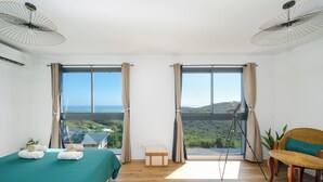 A hotel room with a bed, a small table, a chair, a tripod, and a view of the landscape. - Villa Mansfenil - Le Marin- Sea and forest view (Le Marin)