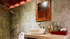Un baño con inodoro blanco, un lavamanos grande de color blanco, un espejo con marco de madera y una zona de ducha.