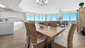 Une cuisine moderne avec des meubles blancs, un îlot central et un coin repas comprenant des chaises en osier et une table en bois.