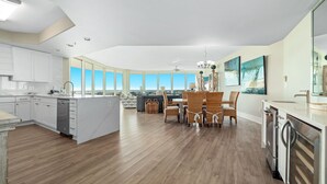 Une cuisine moderne dotée d’un grand îlot central, de meubles blancs et d’un coin repas avec des chaises en osier.