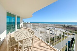 Ein Balkon mit Tisch und Stühlen mit Blick auf einen Strand und einen Parkplatz.