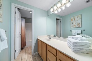 A bathroom with a white sink, wooden cabinets, a mirror with lights, and a towel rack with folded towels. - Beachfront Escape | Gulf-View Balcony, Resort Pools & Iconic Location | BEACHBALL PROPERTIES (Orange Beach)