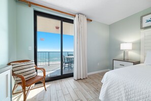 A hotel room with a bed, a chair, a nightstand, a lamp, and a view of the balcony. - Beachfront Escape | Gulf-View Balcony, Resort Pools & Iconic Location | BEACHBALL PROPERTIES (Orange Beach)