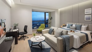 Quarto de hotel moderno com cama grande, sofá, escrivaninha e vista para a cidade.