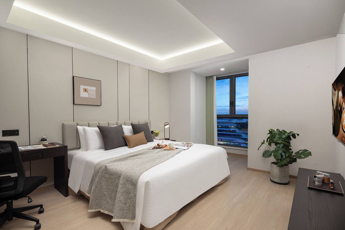 Een moderne hotelkamer met een bed, bureau en een potplant.