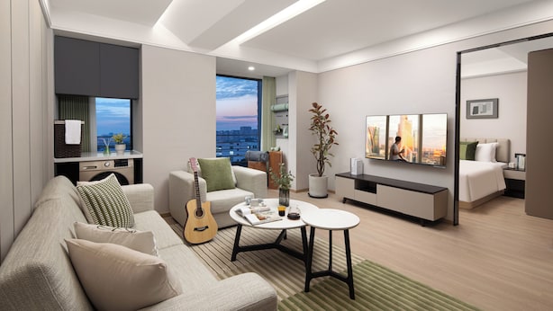 Uma sala de estar moderna com sofá, mesa de centro e uma guitarra. Há vista para a cidade através de uma grande janela.