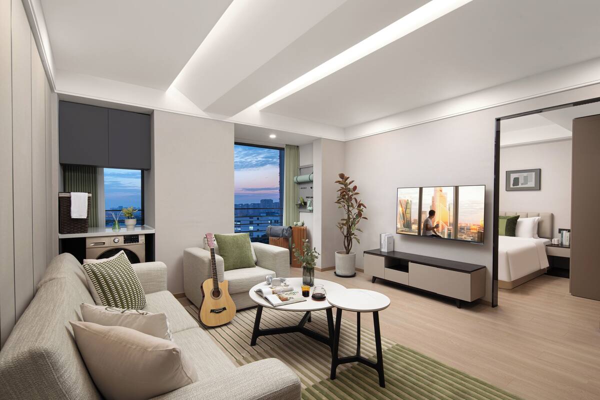 Een moderne woonkamer met een bank, salontafel en een gitaar. Er is uitzicht op de stad door een groot raam.