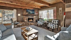 Interior acogedor de una cabaña con chimenea de piedra, sillones a cuadros y un amplio ventanal con vistas a un paisaje pintoresco.