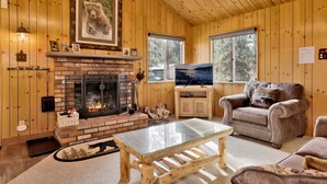 Un intérieur de chalet chaleureux avec une cheminée, des murs en bois, un téléviseur et un coin salon confortable.