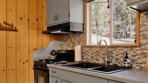 Une cuisine équipée d’une cuisinière, d’un four, d’un évier et d’une fenêtre donnant sur les arbres.