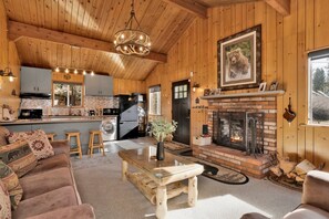 Un intérieur de chalet chaleureux, avec un revêtement en bois, une cheminée, un coin repas et une cuisine équipée d’appareils électroménagers modernes.