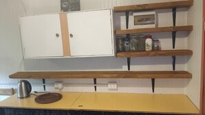 Keittiössä on valkoiset kaapit, puiset hyllyt ja keltainen työtaso.