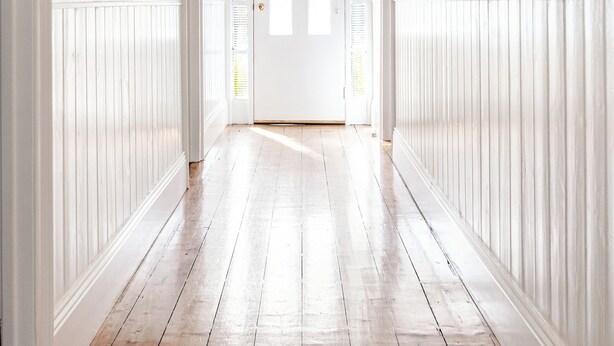 Een gang met witte plinten, een houten vloer en een deur aan het einde.