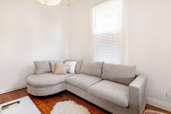 A corner living room with a grey sectional sofa, a white fluffy rug, and a white wall.