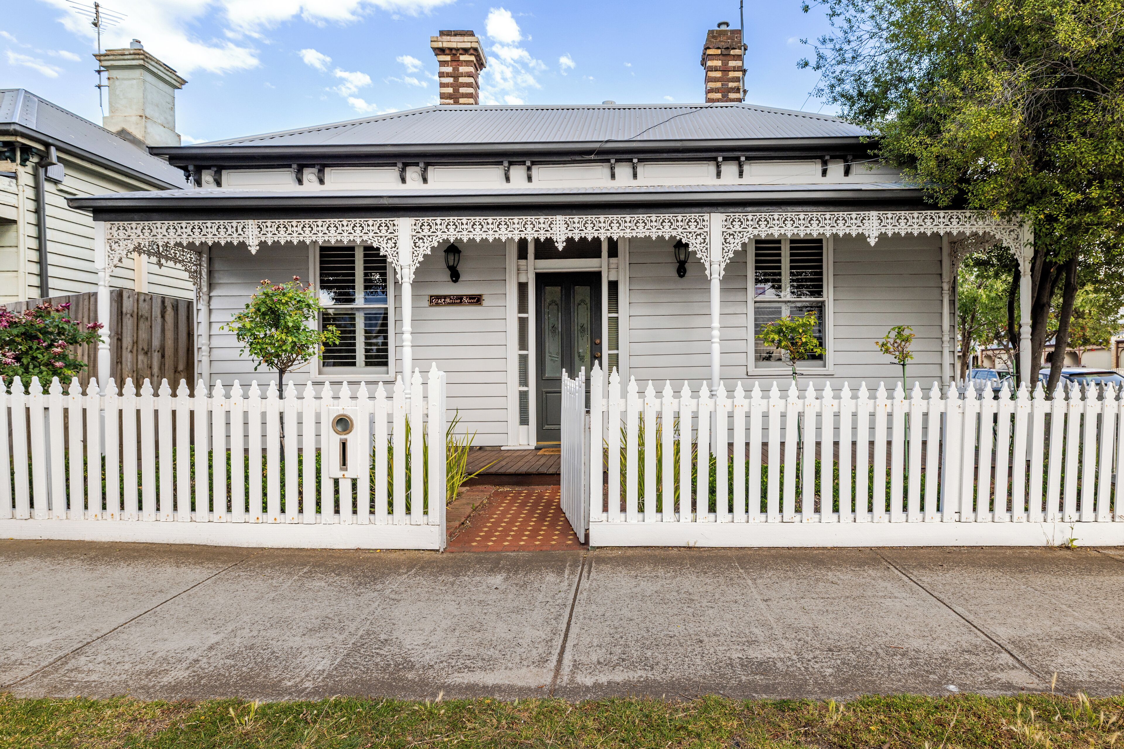 A white house with a picket fence, a front door, and a small porch with decorative railings.