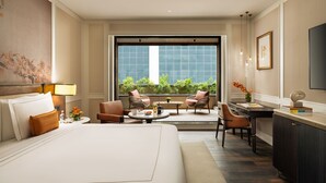 A hotel room with a large bed, a desk, two chairs, a small table, a TV, and a balcony with plants. - Taj Palace, Lucknow (Lucknow)