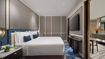 Habitación de hotel moderna con una cama grande, mesitas de noche, un televisor de pantalla plana, un escritorio y un baño visible a través de una puerta abierta.
