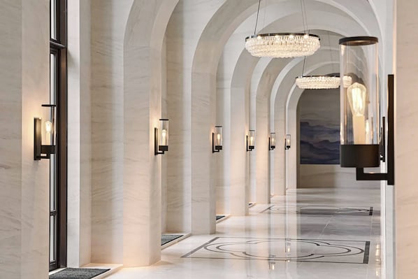 A modern hotel lobby with arched ceilings, chandeliers, and a marble floor.