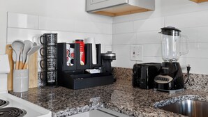 Eine Küche mit einer Kaffeestation, einschließlich Kaffeemaschine, Kaffeemühle und Tassen, sowie einem Mixer auf der Arbeitsfläche.