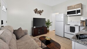 Ein Wohnzimmer mit Sofa, Fernseher und Couchtisch. Es gibt eine Küchenzeile mit Herd, Mikrowelle und Kühlschrank.