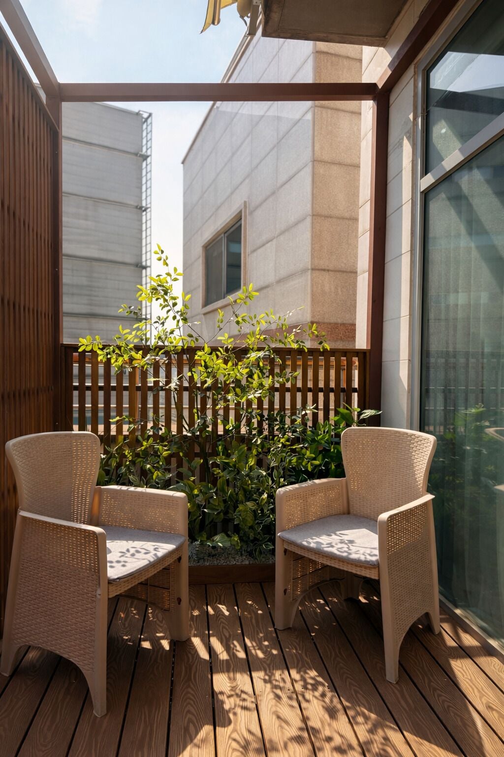 Eine Holzterrasse mit zwei Korbstühlen, einem Holzzaun und einem Gebäude im Hintergrund.