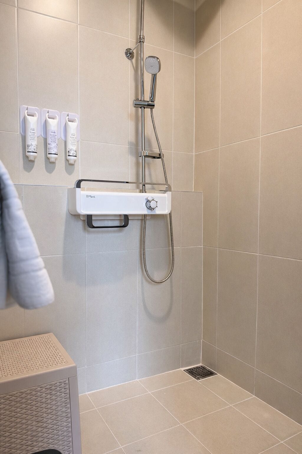 A shower with a handheld showerhead, a wall-mounted control panel, and three toiletries.