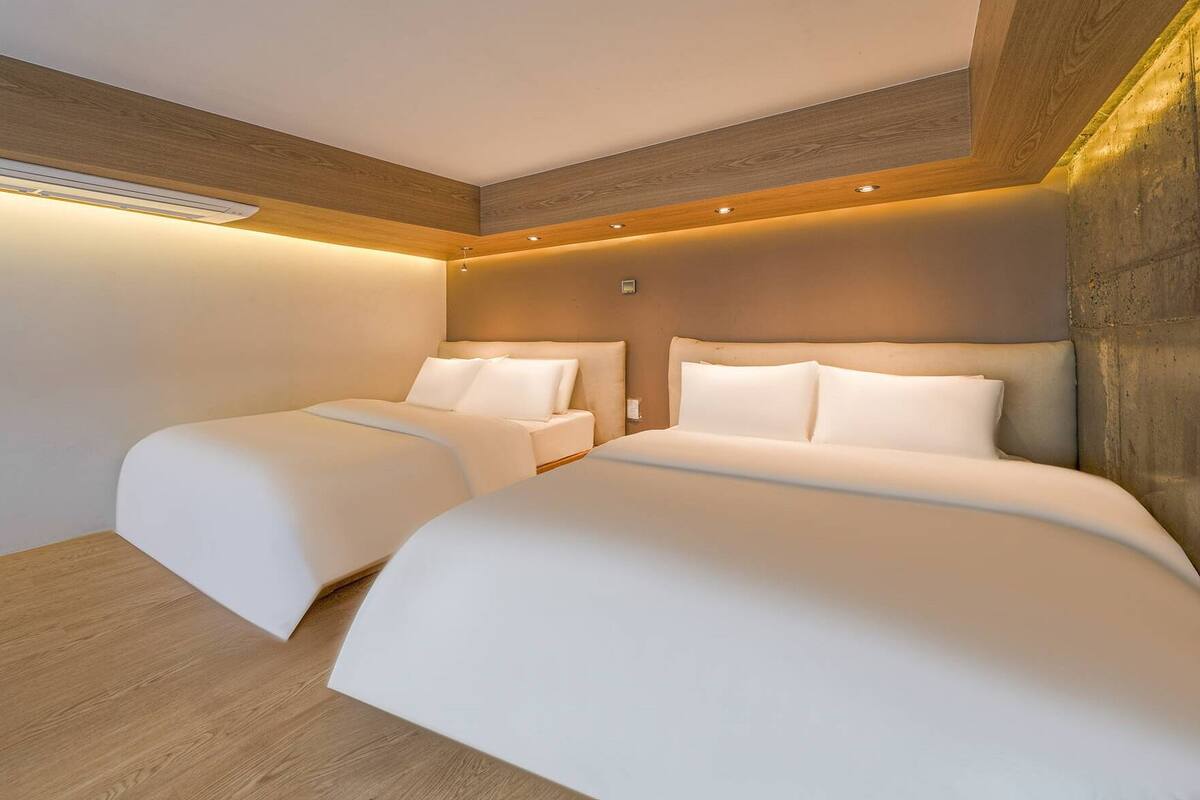 Een moderne hotelkamer met twee bedden, houten lambrisering en inbouwverlichting.