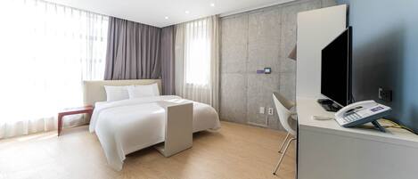 A modern hotel room with a bed, a desk with a phone and a flat-screen TV, a chair, and a large window with curtains.