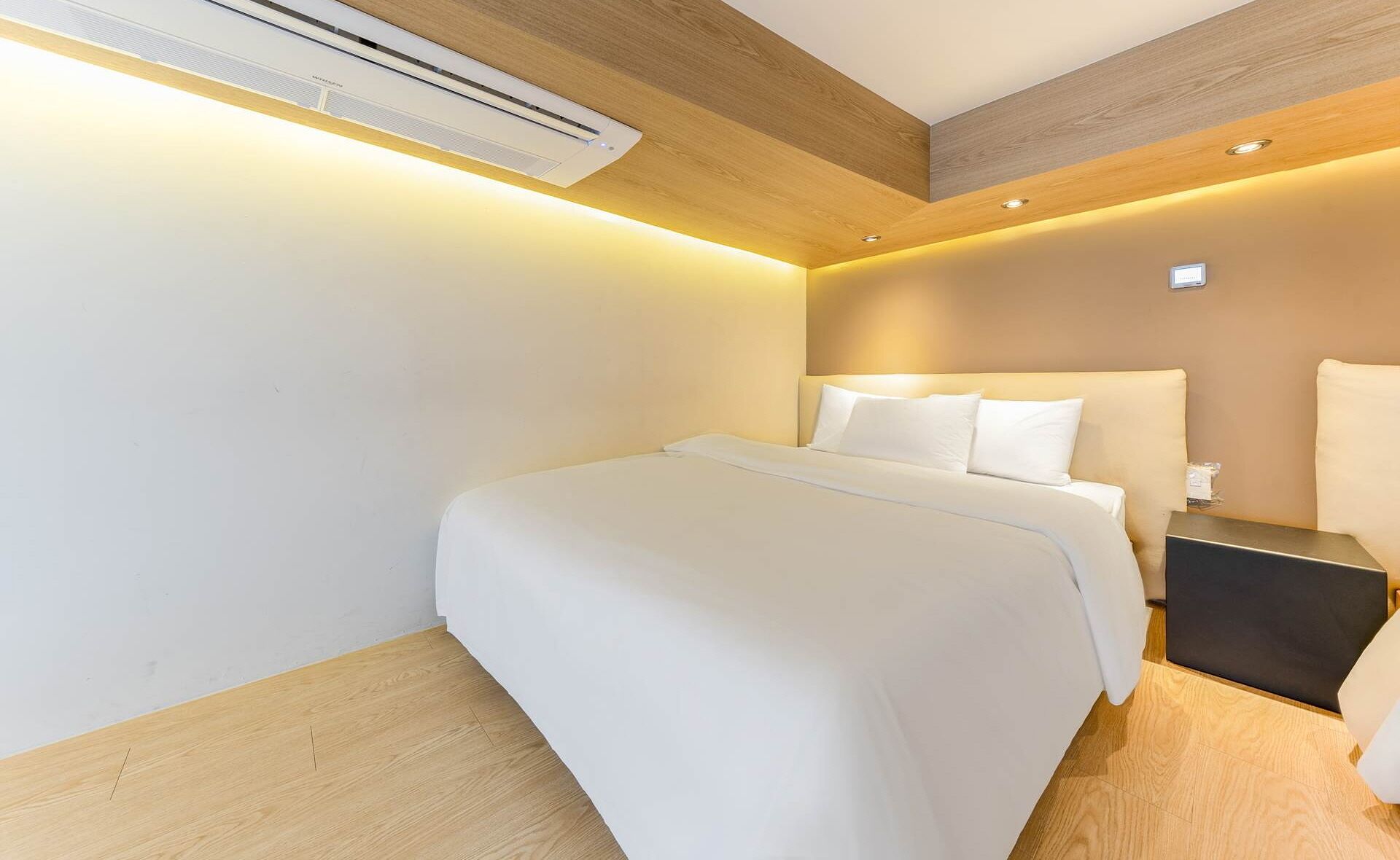 A modern hotel room with a wooden ceiling, a bed with white linens, and a nightstand with a lamp.