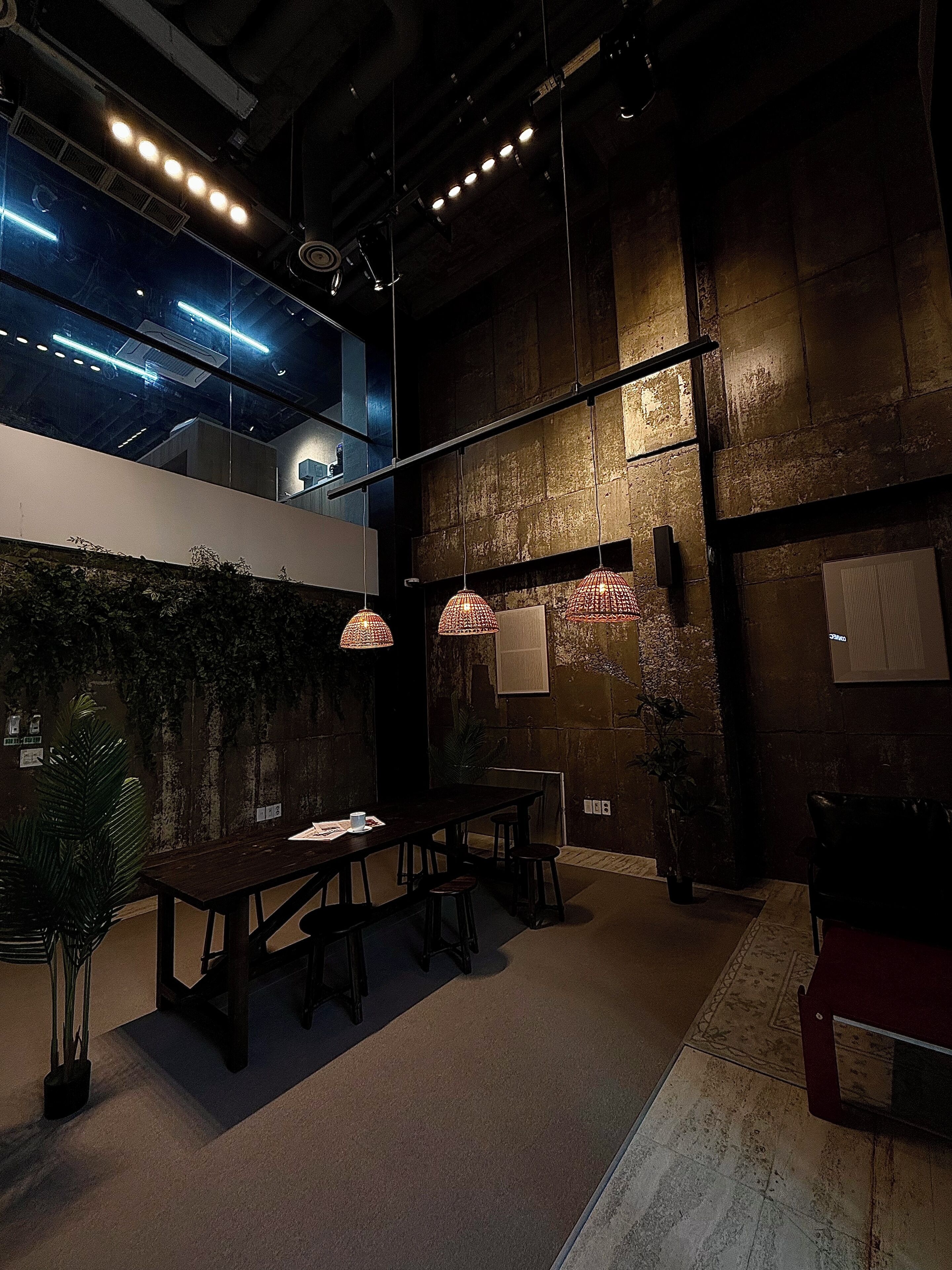 A modern interior with a high ceiling, exposed brick walls, and a dining area with a long table and stools.