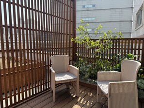 Een houten terras met twee rieten stoelen en een kleine tafel, omgeven door een houten hek en planten.