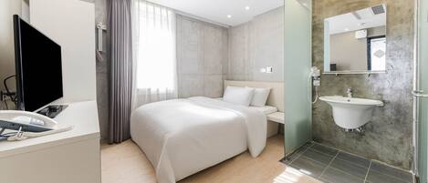 A modern hotel room with a large bed, a bedside table with a phone, a TV, a bathroom with a sink and mirror, and a shower area.