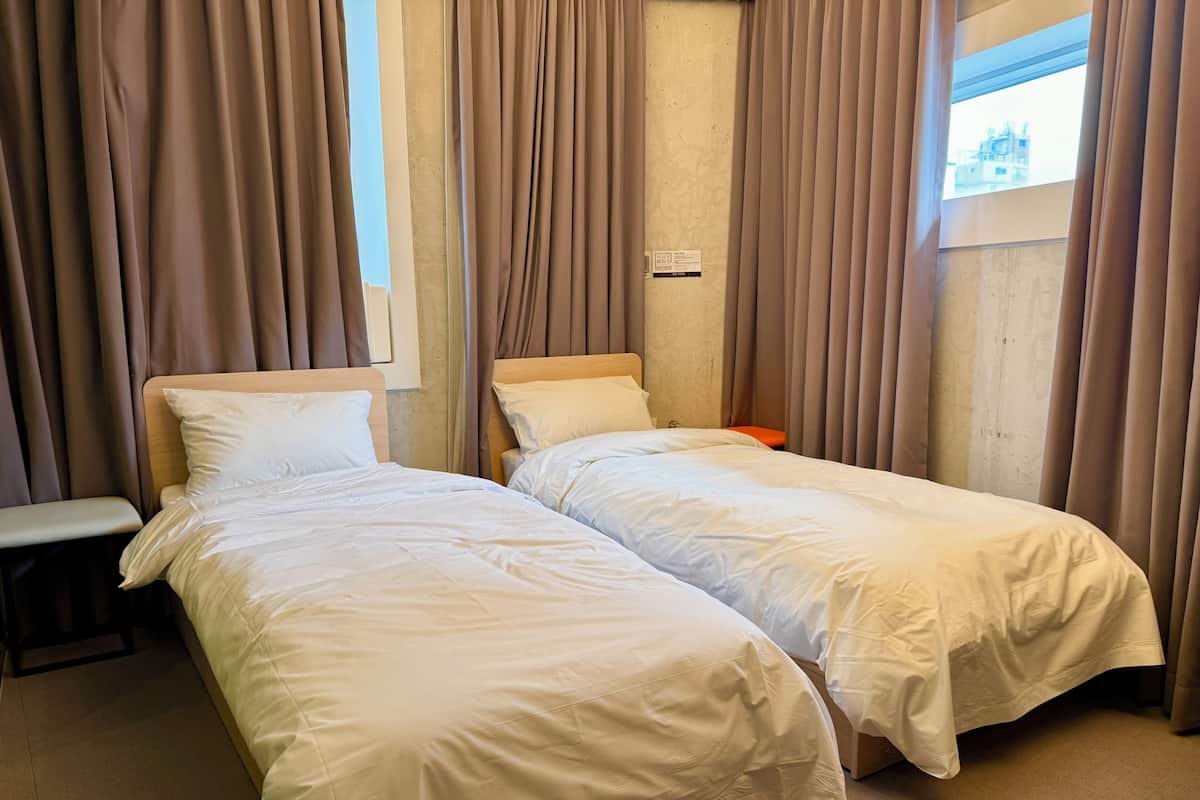 Een hotelkamer met twee eenpersoonsbedden, een tafeltje en een raam met gordijnen.