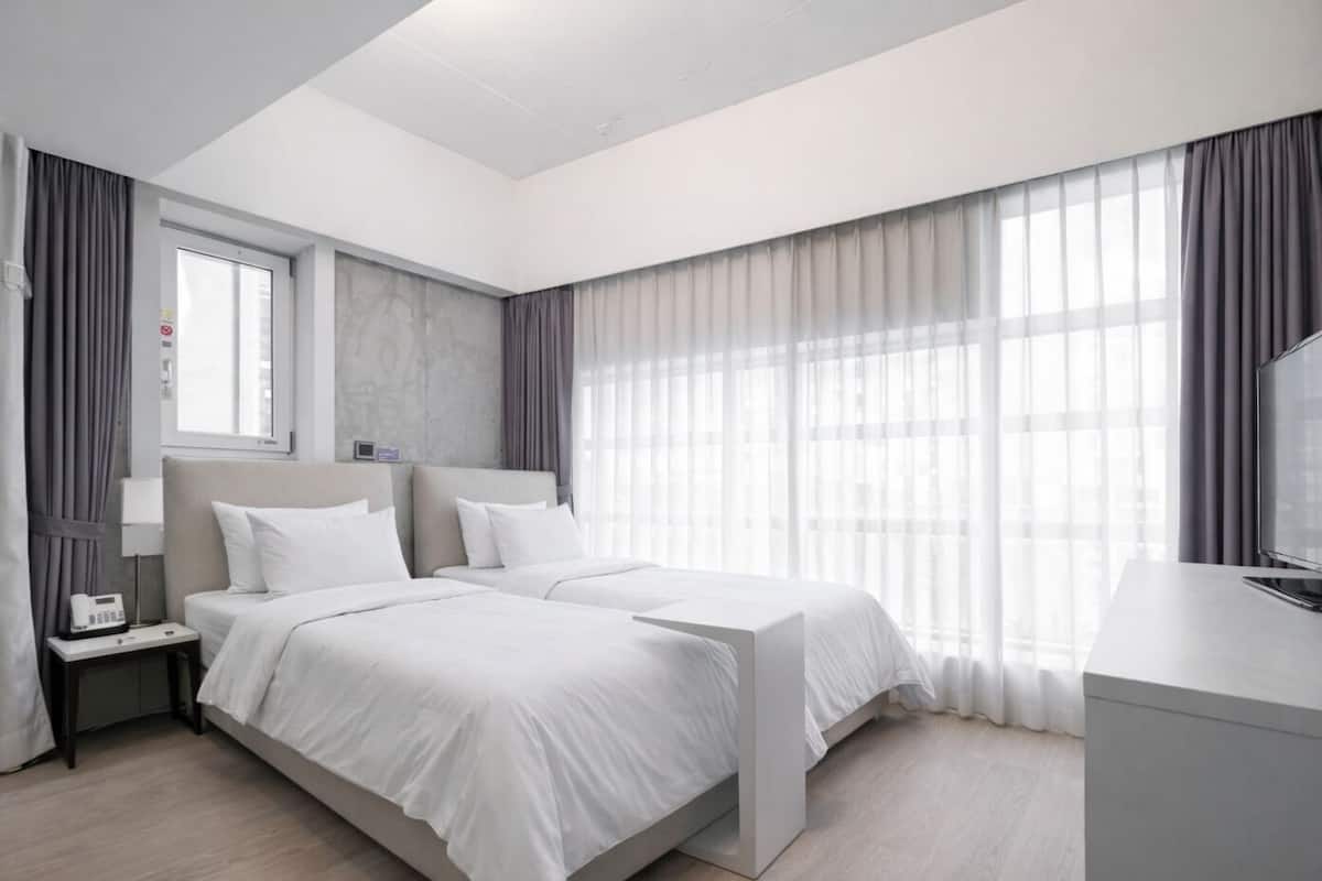 Een moderne hotelkamer met een groot bed, een nachtkastje, een televisie en een raam met gordijnen.