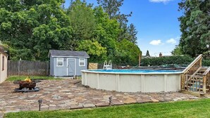 Ein Garten mit Swimmingpool, Feuerstelle, einer kleinen Gartenhütte und einer Holztreppe.