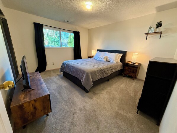 A bedroom with a bed, a TV, a wooden dresser, a desk, a lamp, and a shelf with a plant. - 3BR Near Asante Hospital Medical Pros WIFI and Pool (Medford)