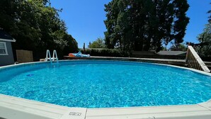 Ein rechteckiger Pool über dem Erdboden mit einer Leiter an einer Seite, umgeben von Bäumen und blauem Himmel.