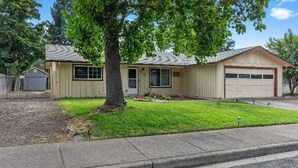 Ein Bungalow mit Garage, Rasen und Baum davor.