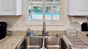 Eine Küche mit doppelter Spüle, einem Fenster mit Blick auf einen Pool und einer Arbeitsplatte mit Geschirrgestell und Seifenspender.