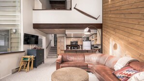 Un salon moderne avec un canapé en cuir, un pouf rond et un escalier menant à un niveau supérieur.
