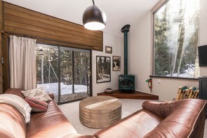 Ein gemütliches Wohnzimmer mit Ledersofas, einem Kamin und einem großen Fenster mit Blick auf Schnee.