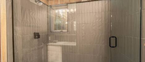 A shower with a glass door, a window, and a tiled floor.