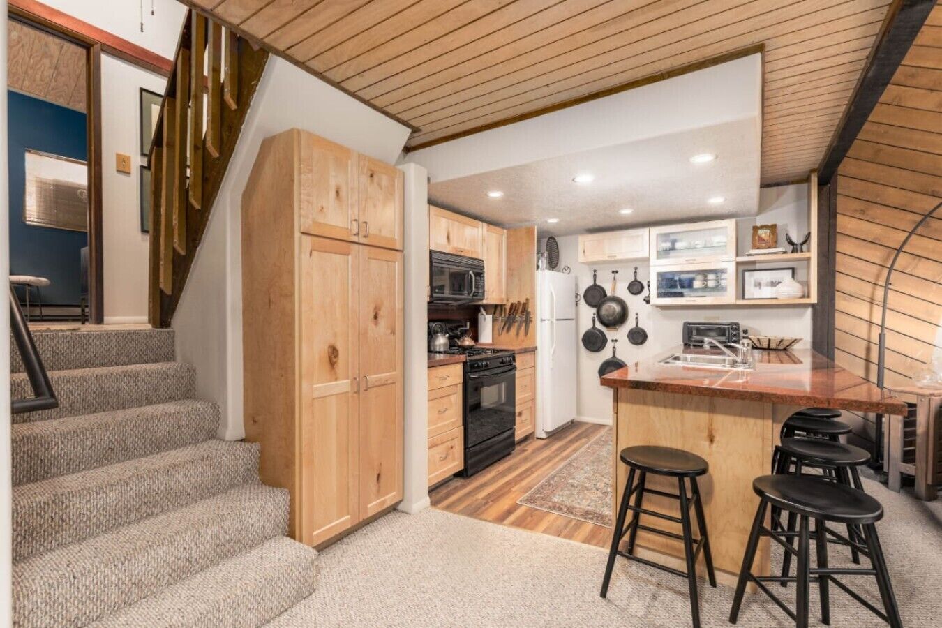 A modern kitchen with wooden cabinets, a central island, and a staircase leading to another level.