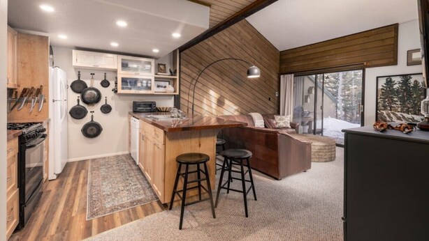 Une cuisine moderne avec un plafond en bois, un coin repas doté d’un bar et une vue sur un paysage enneigé grâce à de grandes fenêtres.