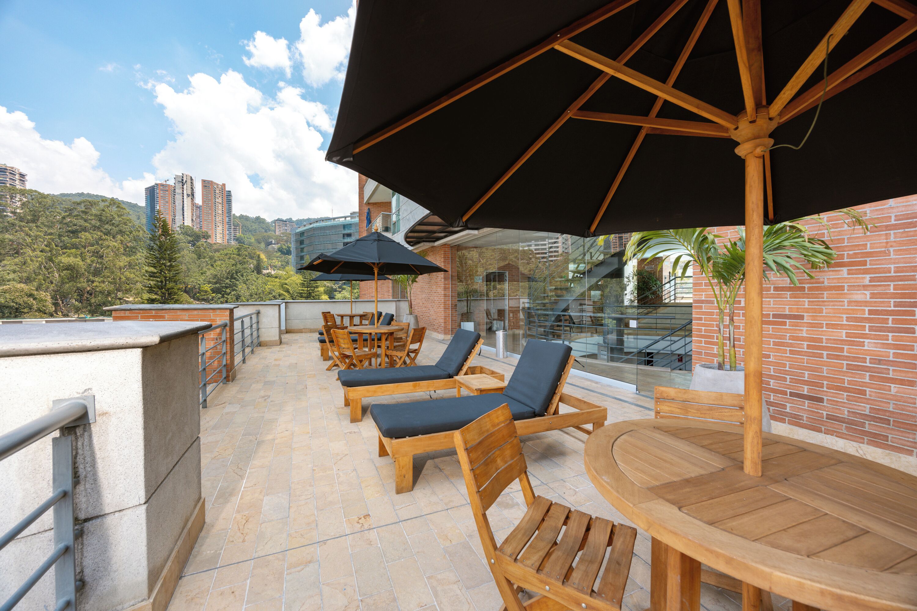 A rooftop terrace with wooden lounge chairs, a round table, and a large umbrella.