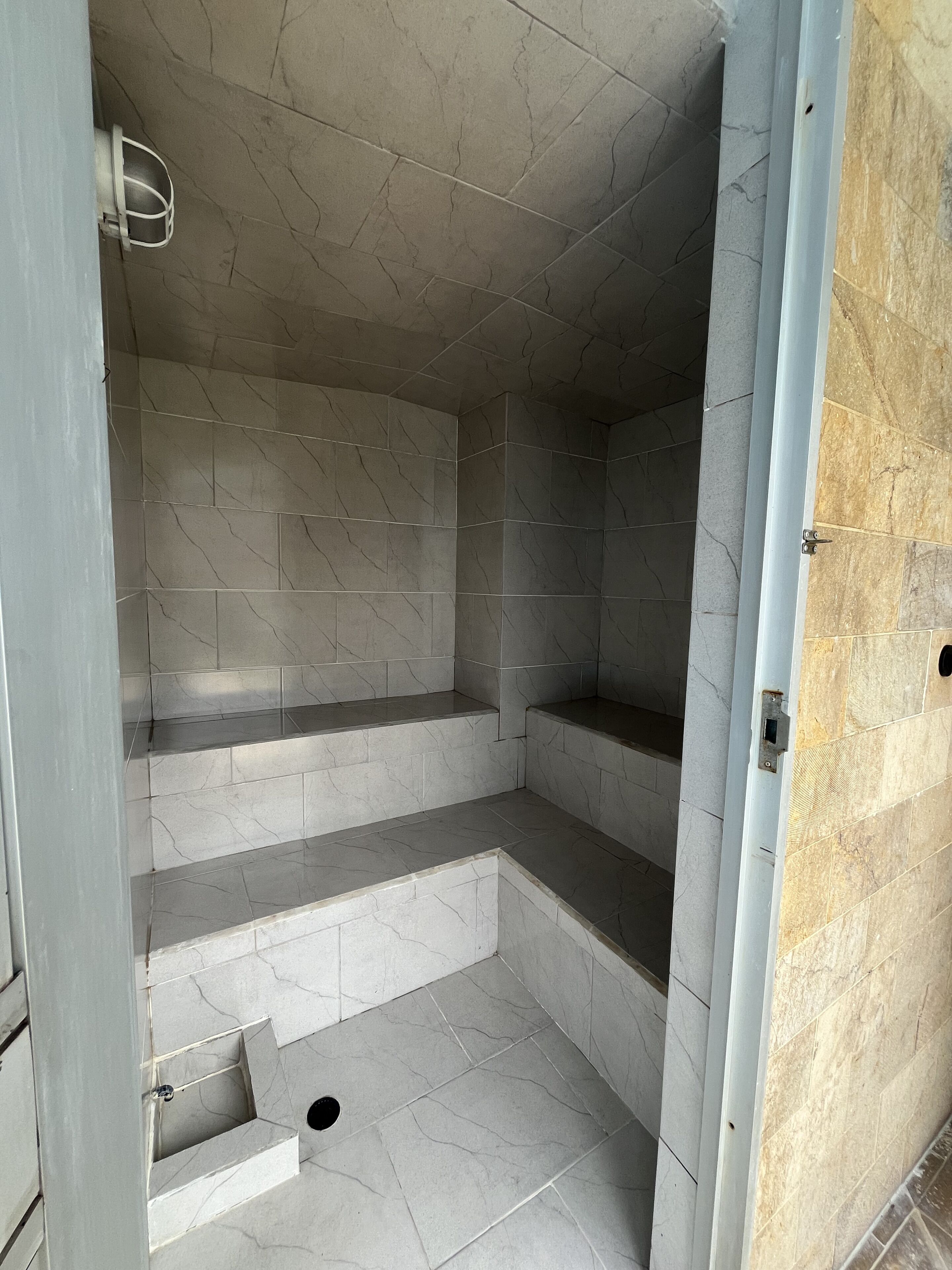 Un espace douche avec des murs et des marches carrelés, une pomme de douche en métal et un drain.