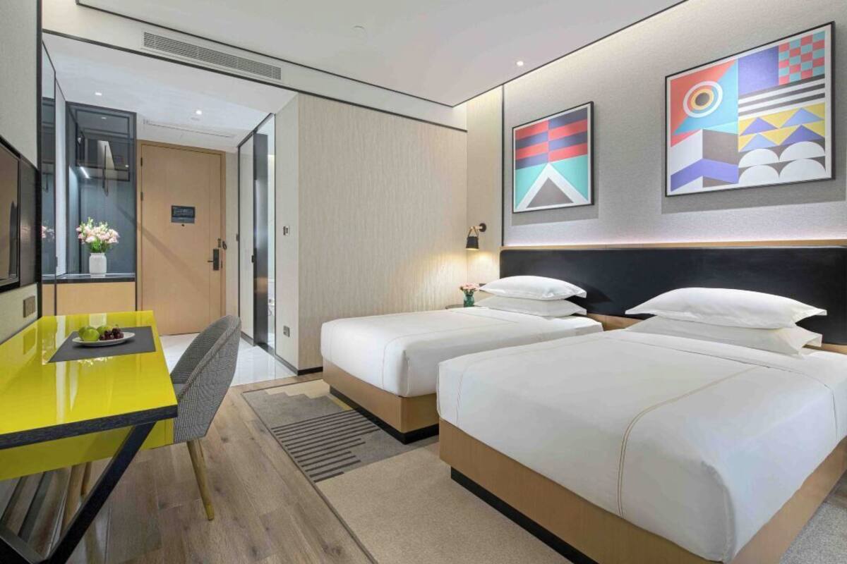 Ein Hotelzimmer mit zwei Betten, einem gelben Tisch, einem Fernseher und Bildern an der Wand.