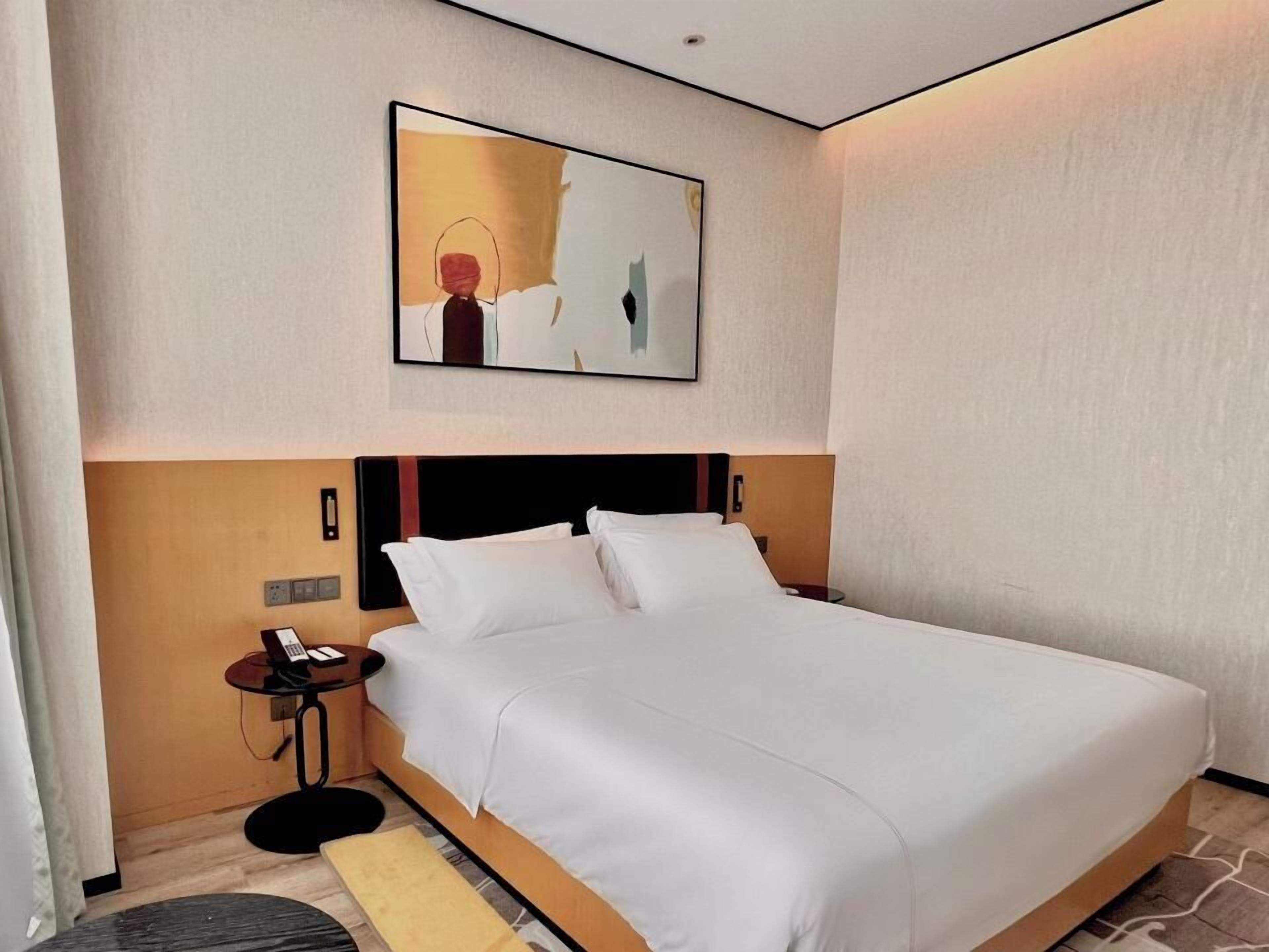 Una habitación de hotel con una cama grande, una mesita de noche con un teléfono y un cuadro en la pared.