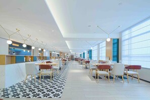 A modern restaurant with a long counter, multiple seating areas, and large windows providing natural light. - The Hotel V Wuxi (Wuxi)