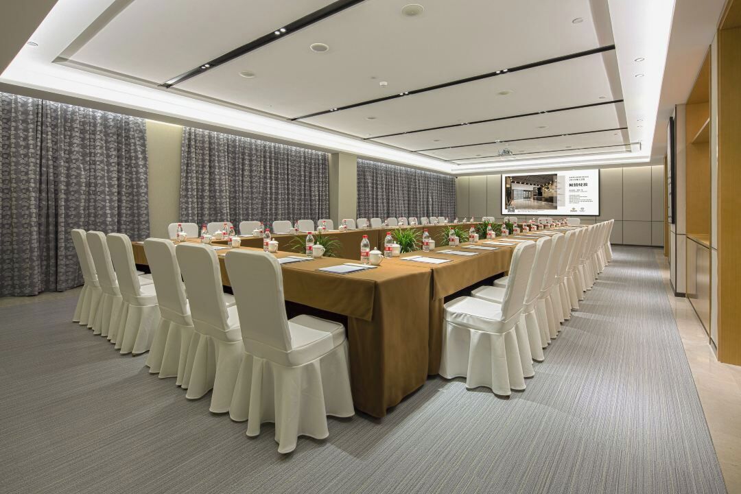 A conference room with a long table, white chairs, and a ceiling with recessed lighting.